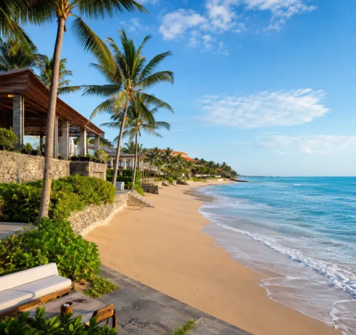 Seminyak, Bali beachfront with golden sand, turquoise sea, swaying palm trees, and luxury seaside villas in clear daylight.