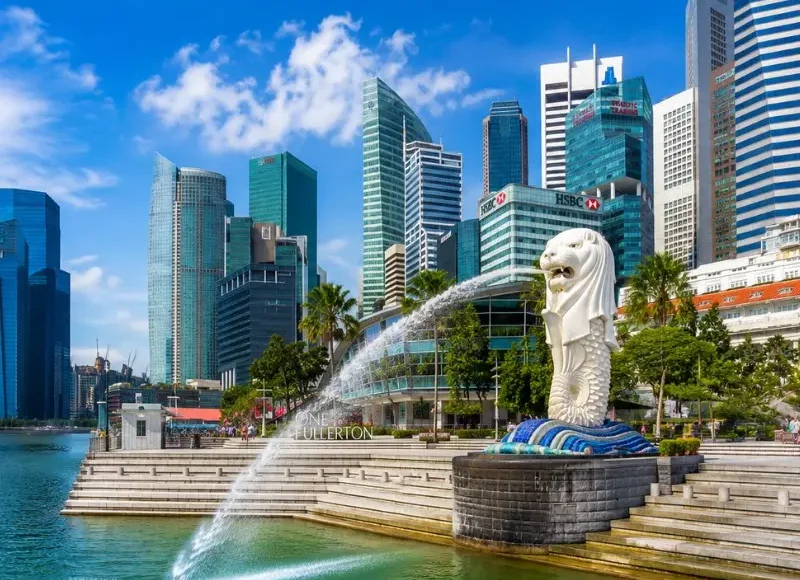Singapore Merlion at Marina Bay with modern skyline, waterfront promenade and bright blue daytime sky