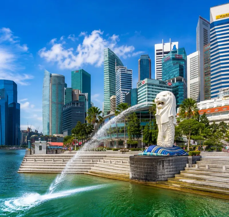 Singapore Merlion at Marina Bay with modern skyline, waterfront promenade and bright blue daytime sky