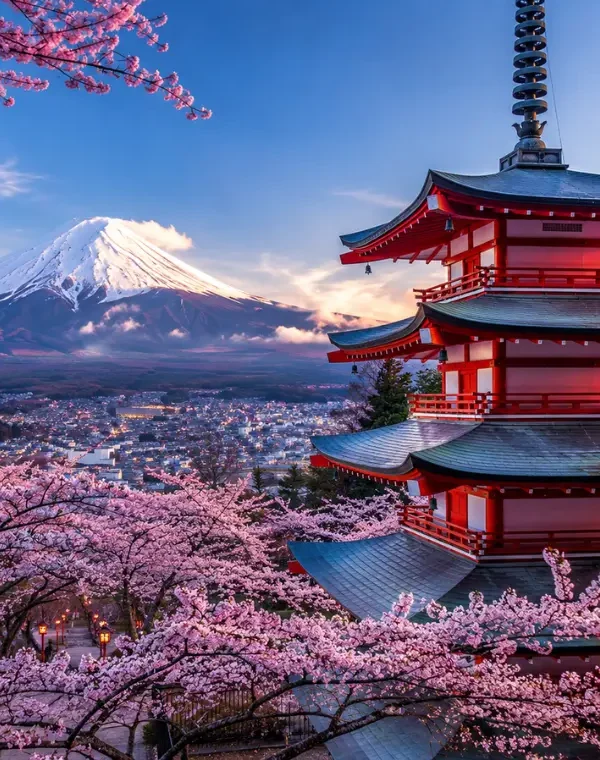 Bright Tokyo view with pink cherry blossom trees, a red temple, and snow-capped Mount Fuji in the background.