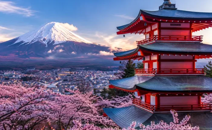 Bright Tokyo view with pink cherry blossom trees, a red temple, and snow-capped Mount Fuji in the background.