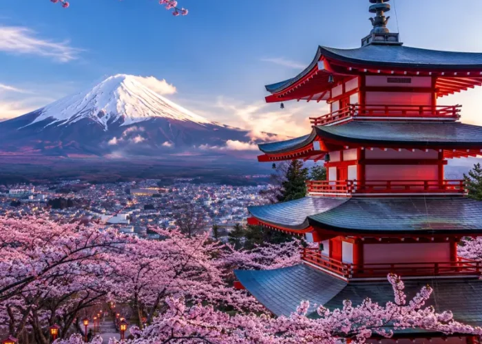 Bright Tokyo view with pink cherry blossom trees, a red temple, and snow-capped Mount Fuji in the background.