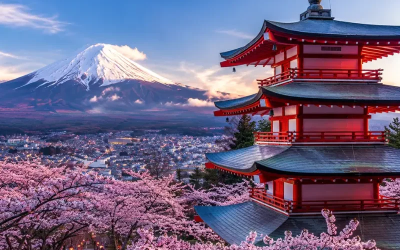 Bright Tokyo view with pink cherry blossom trees, a red temple, and snow-capped Mount Fuji in the background.