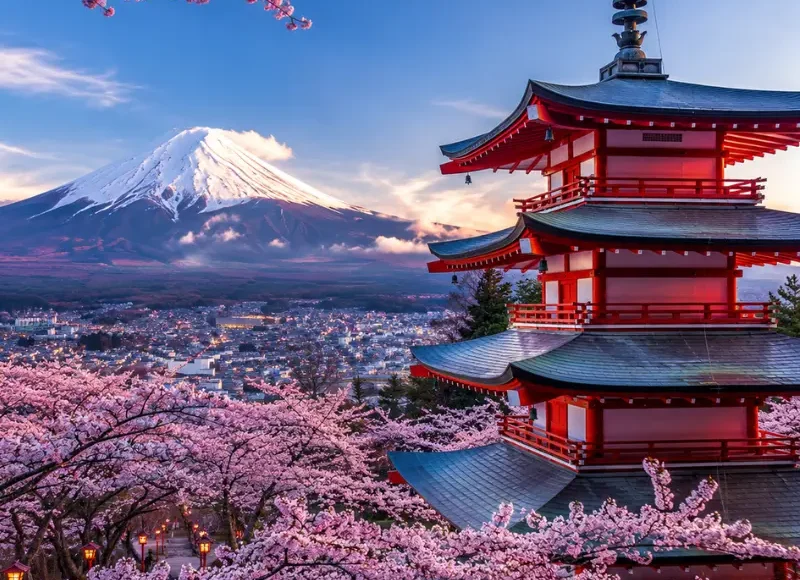 Bright Tokyo view with pink cherry blossom trees, a red temple, and snow-capped Mount Fuji in the background.
