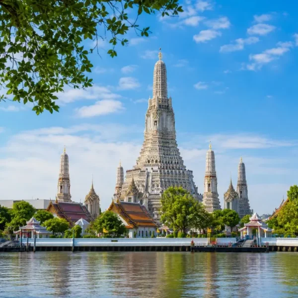 Wat Arun temple in Bangkok beside the Chao Phraya River under bright blue daytime sky