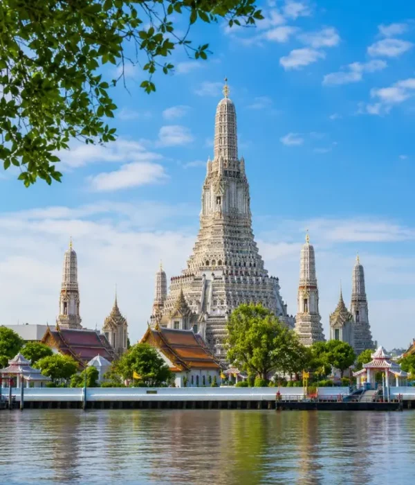 Wat Arun temple in Bangkok beside the Chao Phraya River under bright blue daytime sky