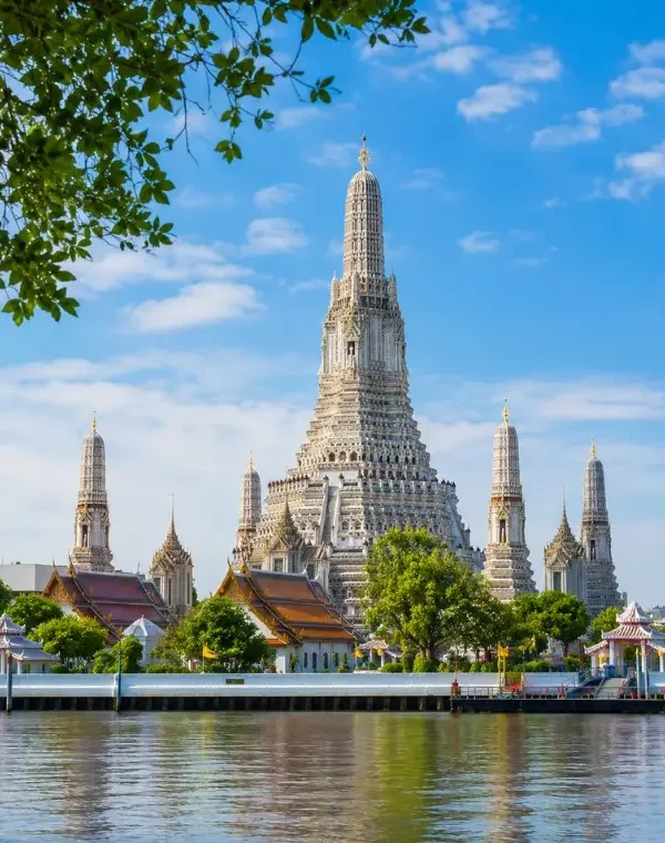 Wat Arun temple in Bangkok beside the Chao Phraya River under bright blue daytime sky