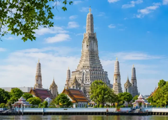 Wat Arun temple in Bangkok beside the Chao Phraya River under bright blue daytime sky