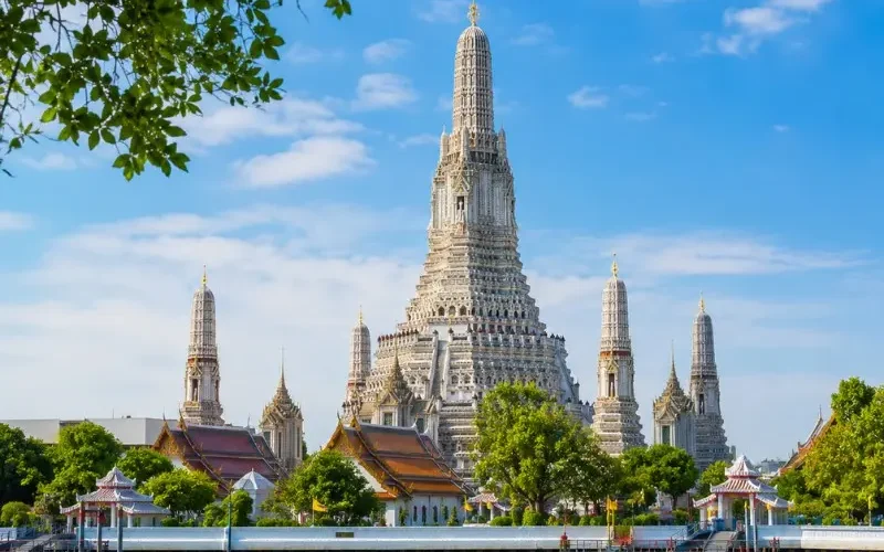 Wat Arun temple in Bangkok beside the Chao Phraya River under bright blue daytime sky
