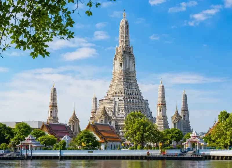 Wat Arun temple in Bangkok beside the Chao Phraya River under bright blue daytime sky