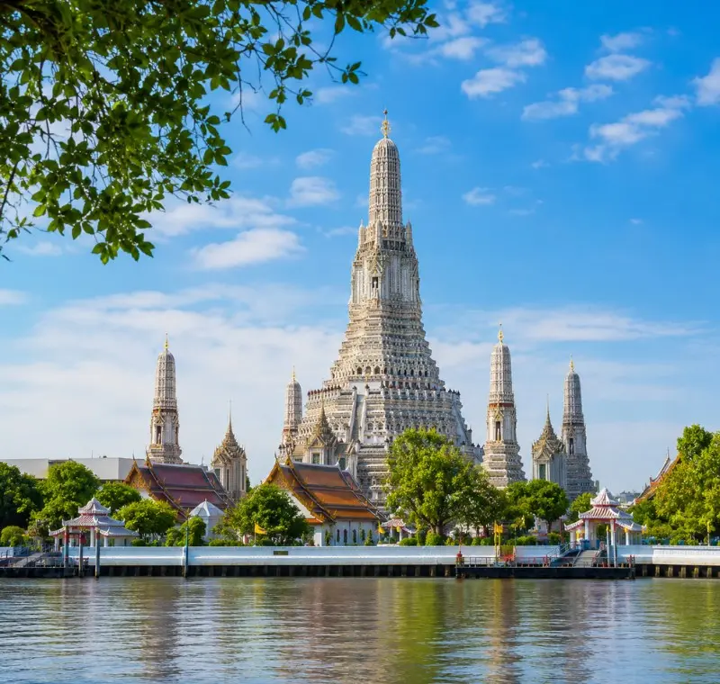 Wat Arun temple in Bangkok beside the Chao Phraya River under bright blue daytime sky