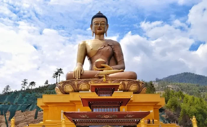 Large Buddha Dordenma statue in Thimphu Bhutan with golden base, forested hills, blue sky, and clouds.