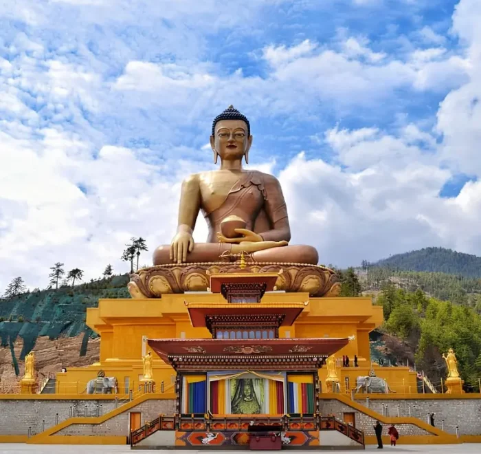 Large Buddha Dordenma statue in Thimphu Bhutan with golden base, forested hills, blue sky, and clouds.