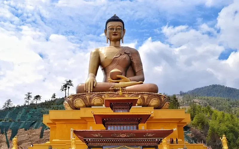 Large Buddha Dordenma statue in Thimphu Bhutan with golden base, forested hills, blue sky, and clouds.