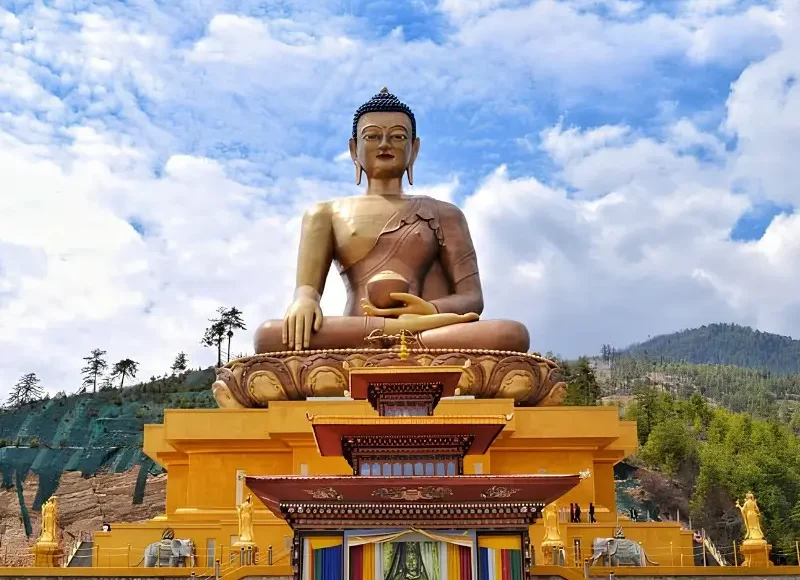 Large Buddha Dordenma statue in Thimphu Bhutan with golden base, forested hills, blue sky, and clouds.