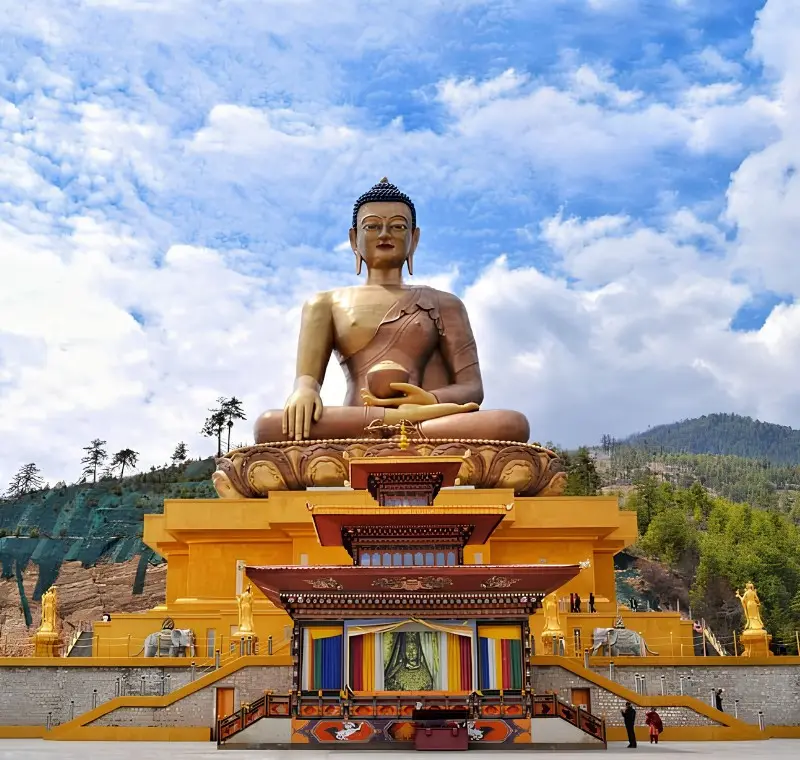 Large Buddha Dordenma statue in Thimphu Bhutan with golden base, forested hills, blue sky, and clouds.