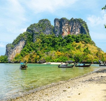 Limestone karst cliffs and lush greenery along the tropical shoreline in Thailand, representing scenic travel destinations in Southeast Asia.