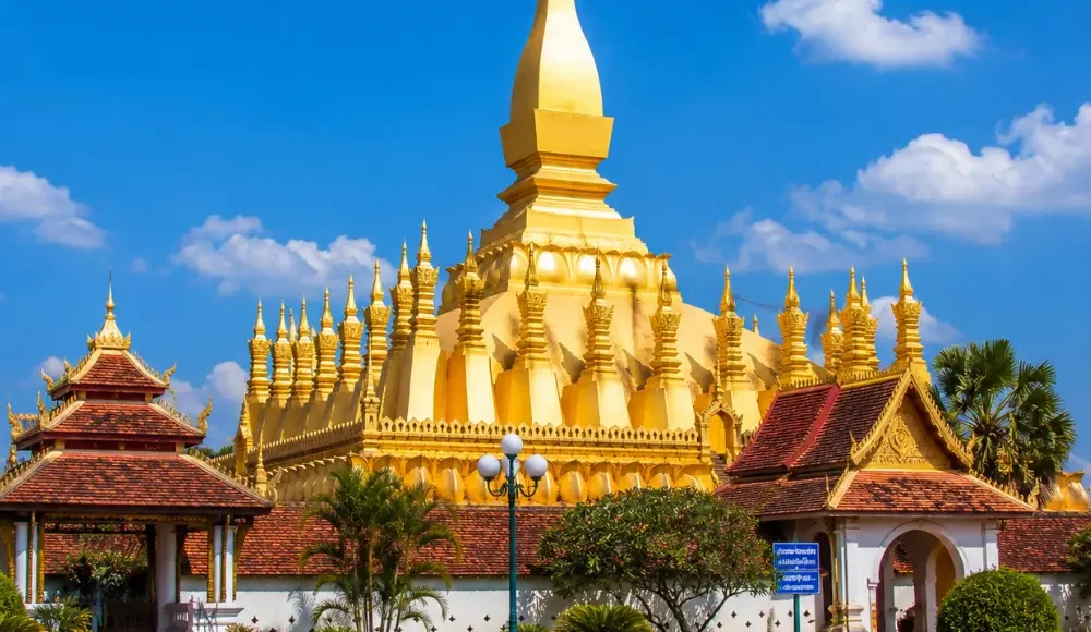 Vientiane Laos with Pha That Luang golden stupa, peaceful gardens, blue sky, and a premium cultural travel atmosphere.