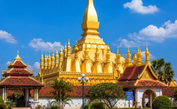 Vientiane Laos with Pha That Luang golden stupa, peaceful gardens, blue sky, and a premium cultural travel atmosphere.