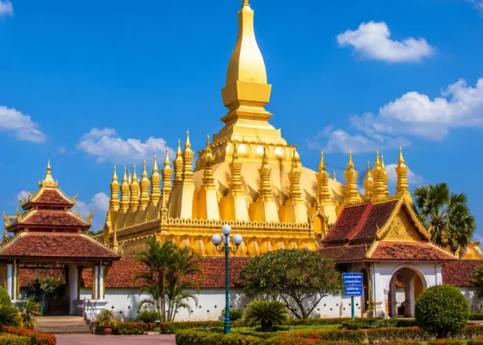 Vientiane Laos with Pha That Luang golden stupa, peaceful gardens, blue sky, and a premium cultural travel atmosphere.