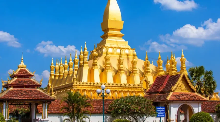 Vientiane Laos with Pha That Luang golden stupa, peaceful gardens, blue sky, and a premium cultural travel atmosphere.