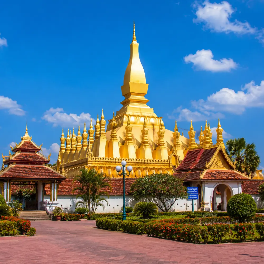 Vientiane Laos with Pha That Luang golden stupa, peaceful gardens, blue sky, and a premium cultural travel atmosphere.
