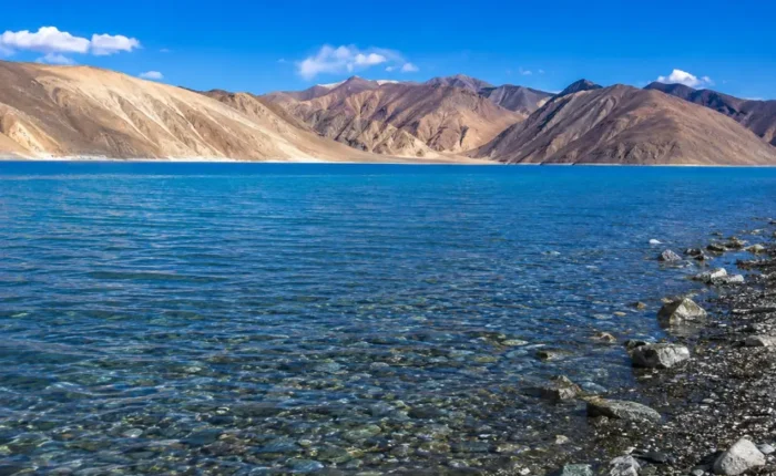 Crystal-clear Pangong Lake in Ladakh with turquoise blue water, rocky shoreline, and barren Himalayan mountains.