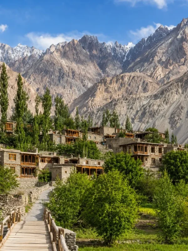 Scenic Turtuk village in Ladakh with traditional stone houses, wooden bridge, green trees, and rugged mountain peaks.