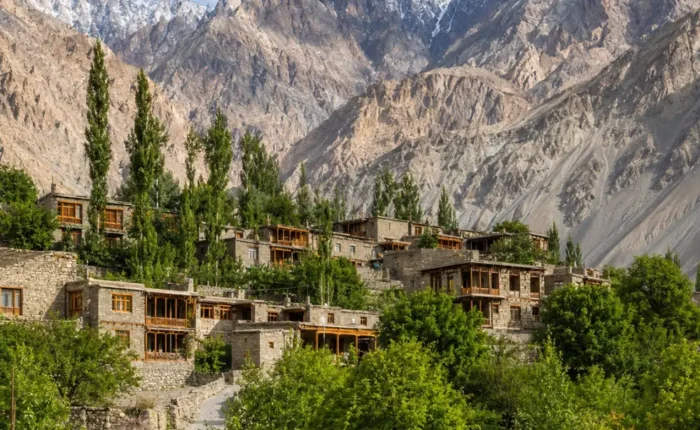Scenic Turtuk village in Ladakh with traditional stone houses, wooden bridge, green trees, and rugged mountain peaks.