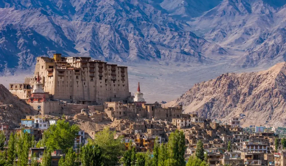 Scenic Leh town in Ladakh with historic palace, green valley, traditional buildings, and snow-capped mountains.