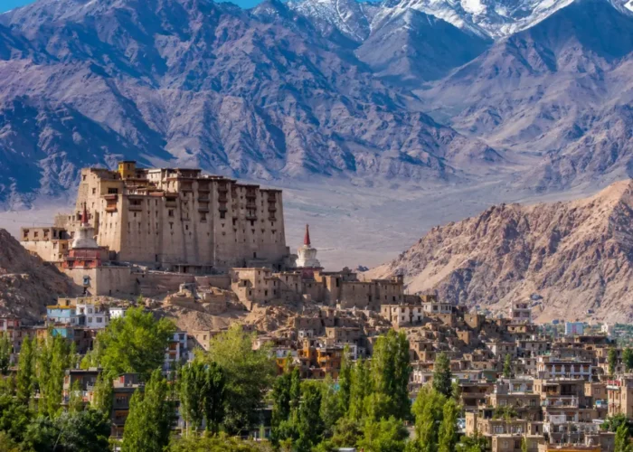 Scenic Leh town in Ladakh with historic palace, green valley, traditional buildings, and snow-capped mountains.