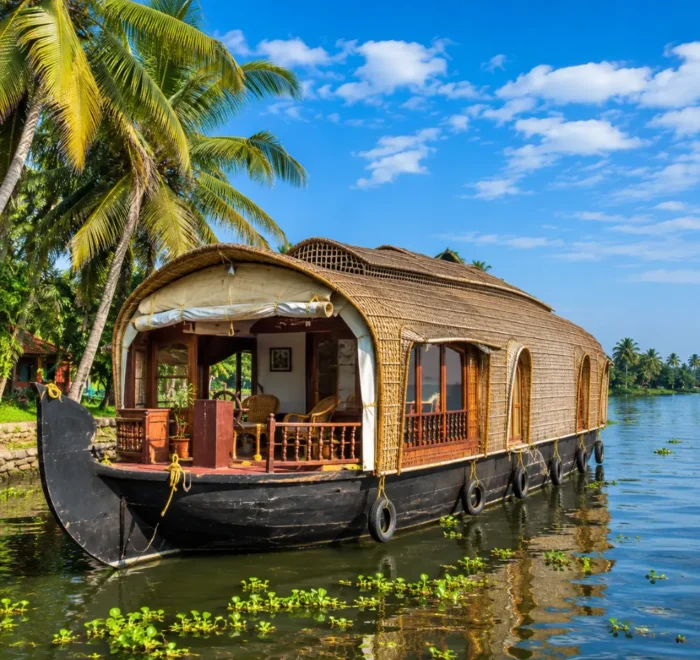 Alleppey houseboat floating on peaceful Kerala backwaters with coconut palms and clear morning daylight.