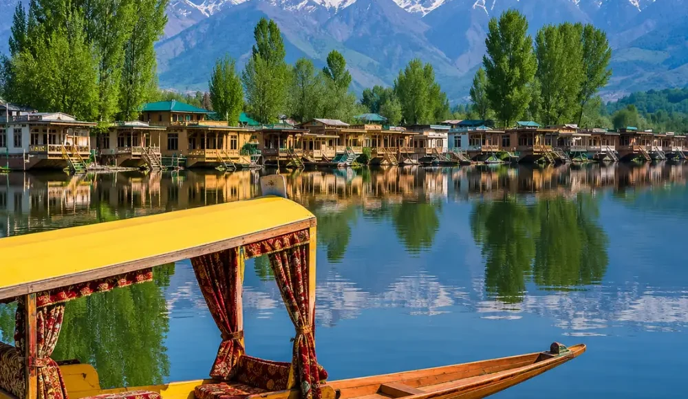 Beautiful Srinagar Dal Lake view with colorful shikara, houseboats, calm water reflections, and snow-capped mountains.