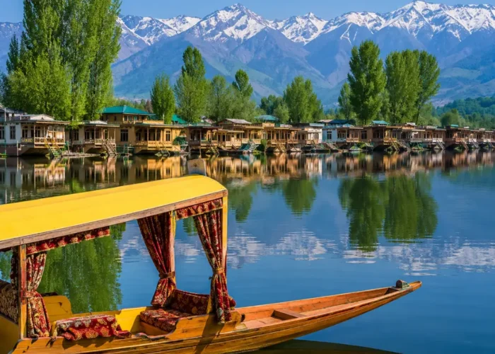 Beautiful Srinagar Dal Lake view with colorful shikara, houseboats, calm water reflections, and snow-capped mountains.