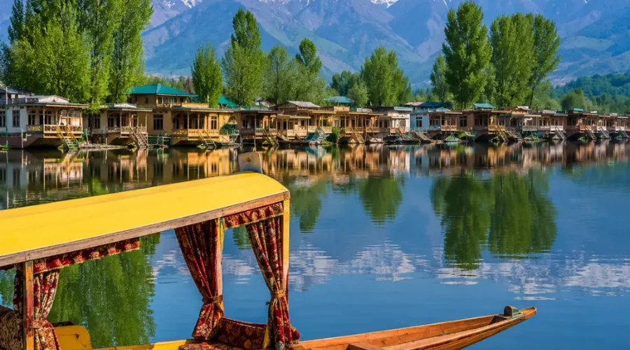 Beautiful Srinagar Dal Lake view with colorful shikara, houseboats, calm water reflections, and snow-capped mountains.