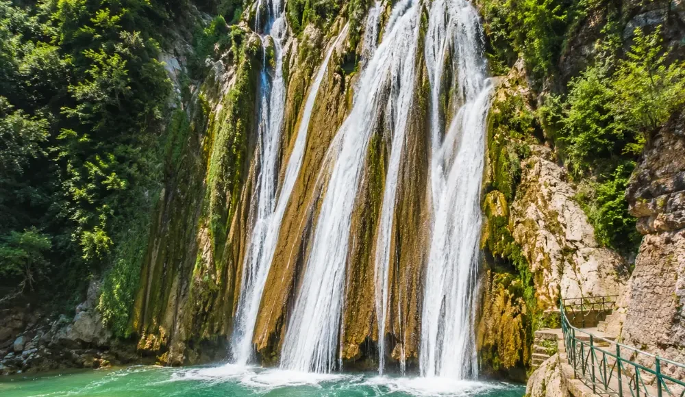 Bright morning view of Kempty Falls in Mussoorie with clear cascading water, rocky cliffs, and lush green hills