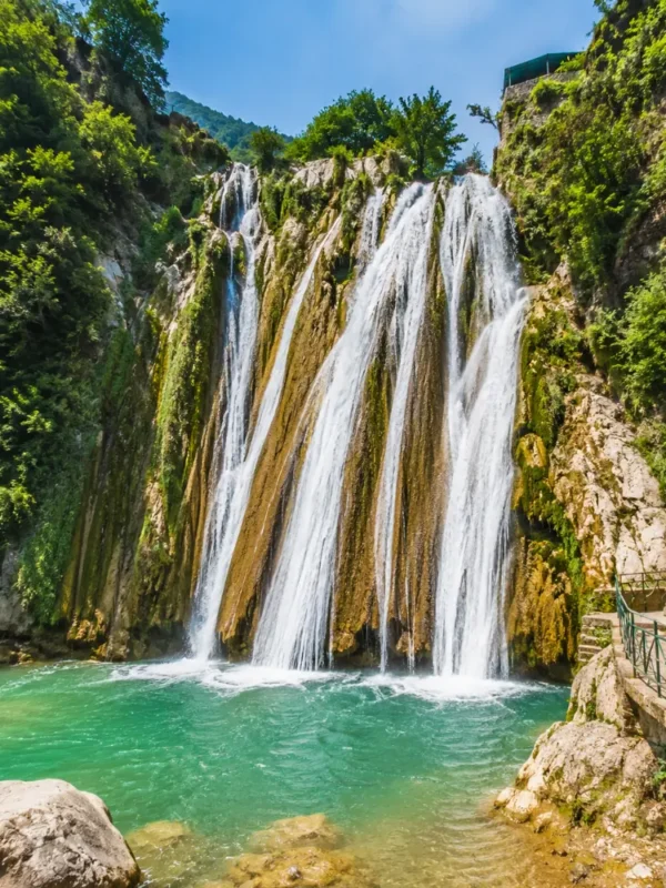 Bright morning view of Kempty Falls in Mussoorie with clear cascading water, rocky cliffs, and lush green hills