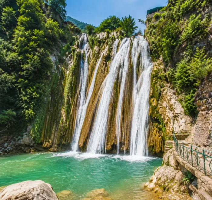 Bright morning view of Kempty Falls in Mussoorie with clear cascading water, rocky cliffs, and lush green hills