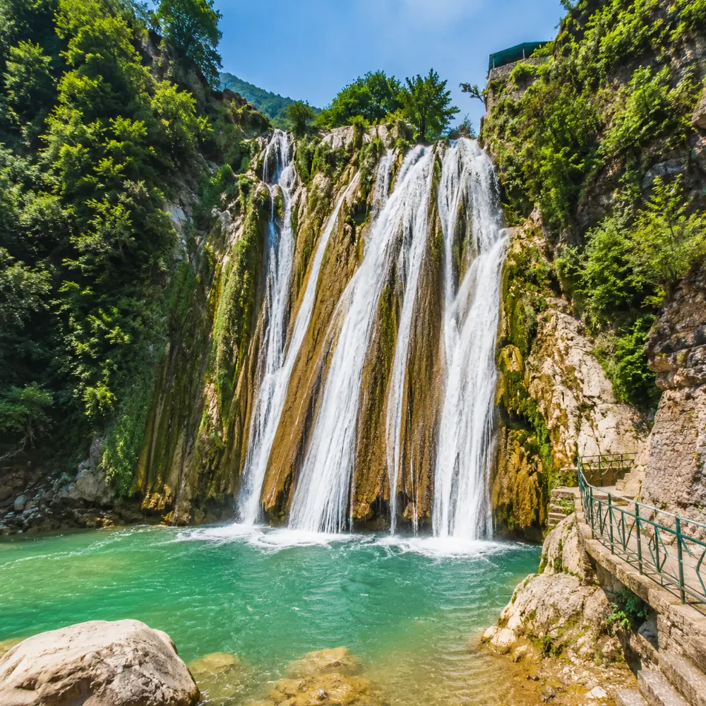 Bright morning view of Kempty Falls in Mussoorie with clear cascading water, rocky cliffs, and lush green hills