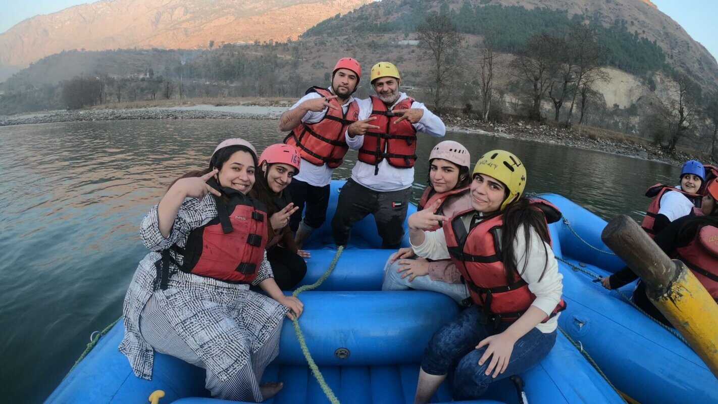Adventurous group enjoying river rafting in scenic mountain landscape, wearing safety gear and helmets, capturing thrilling outdoor adventure in India.