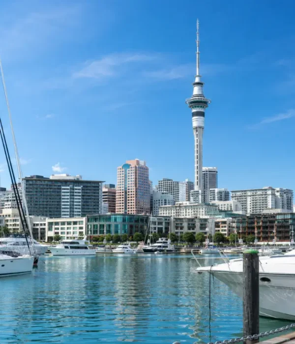 Bright daytime view of Auckland waterfront with Sky Tower, modern skyline, luxury yachts, and calm marina waters.