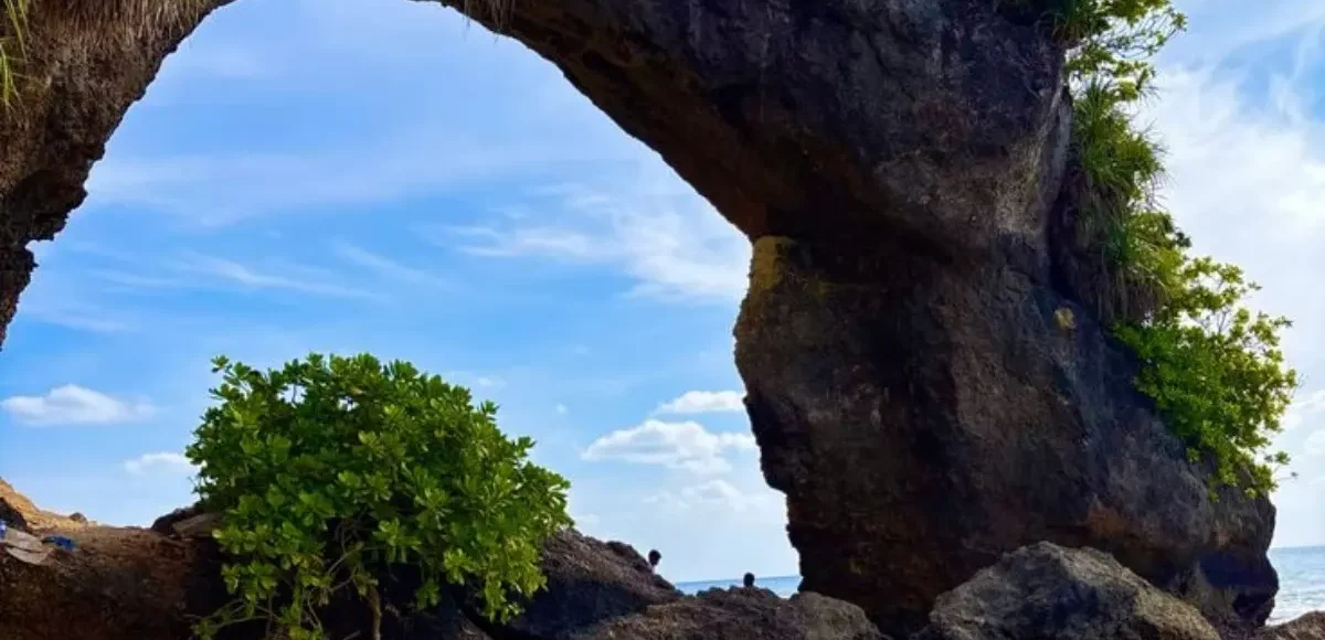 Natural rock bridge in Andaman with blue sky, sea waves, coastal rocks and tropical island scenery