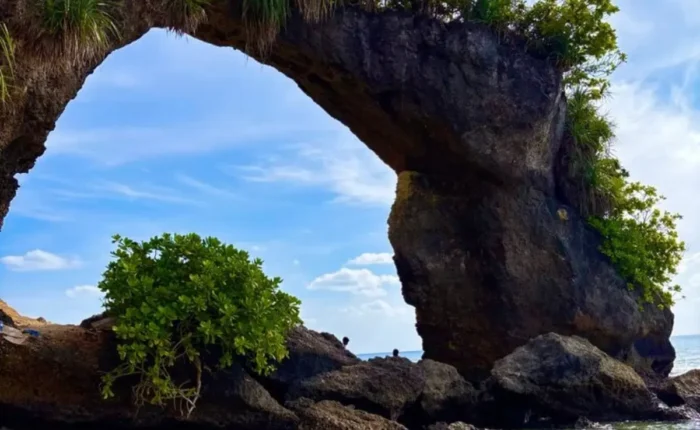 Natural rock bridge in Andaman with blue sky, sea waves, coastal rocks and tropical island scenery