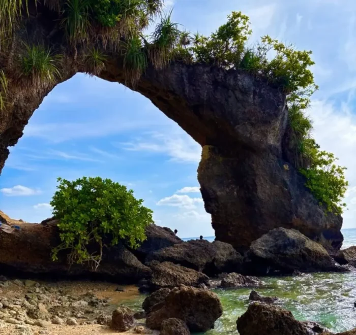 Natural rock bridge in Andaman with blue sky, sea waves, coastal rocks and tropical island scenery