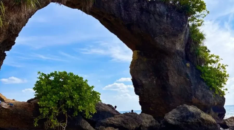 Natural rock bridge in Andaman with blue sky, sea waves, coastal rocks and tropical island scenery