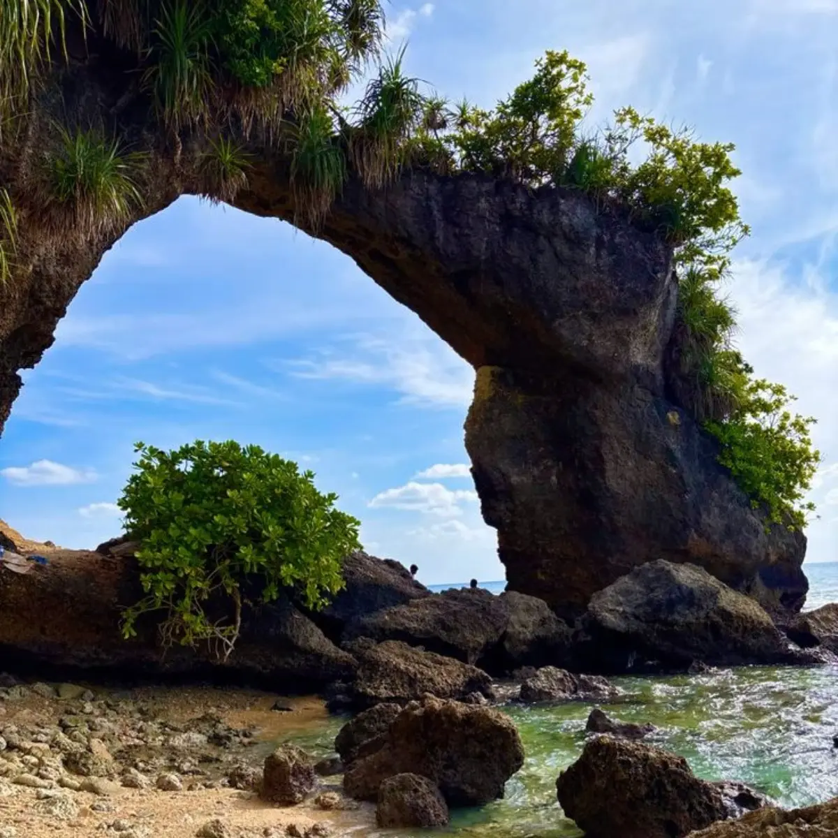 Natural rock bridge in Andaman with blue sky, sea waves, coastal rocks and tropical island scenery