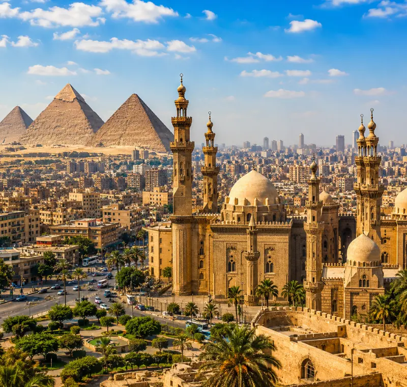 Bright daytime view of Cairo with historic mosque architecture, city skyline, palm trees, and Giza pyramids.