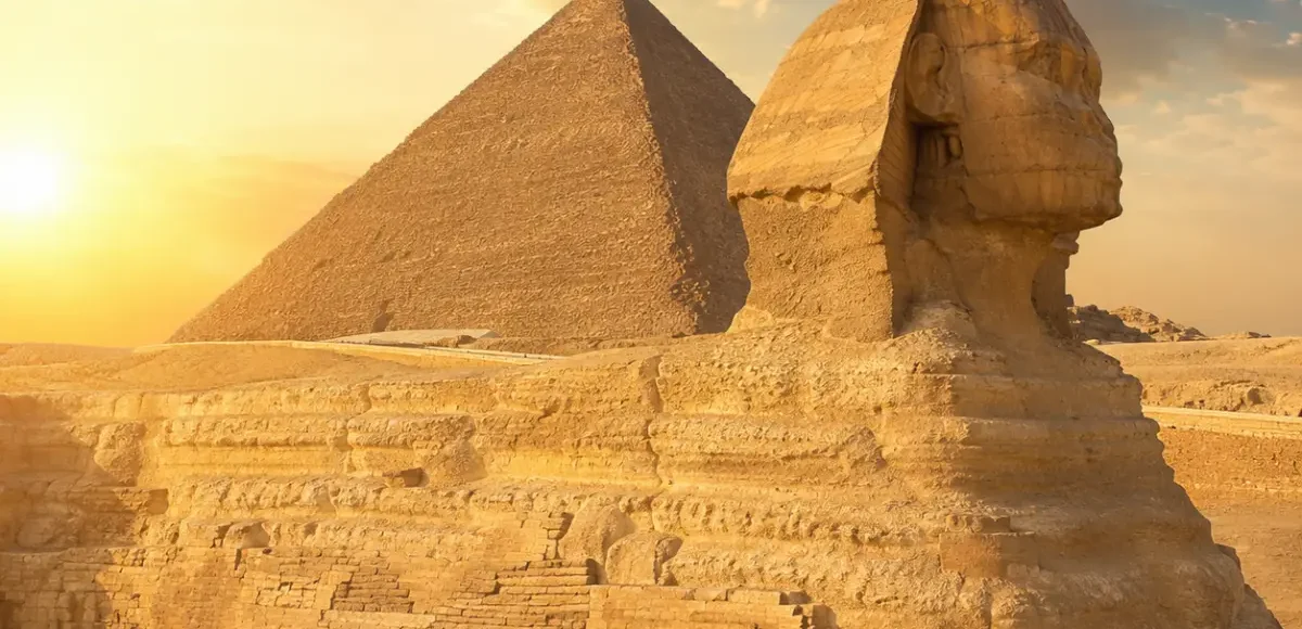 Great Sphinx of Giza with the Pyramid of Khafre in the background under warm golden light in Egypt.