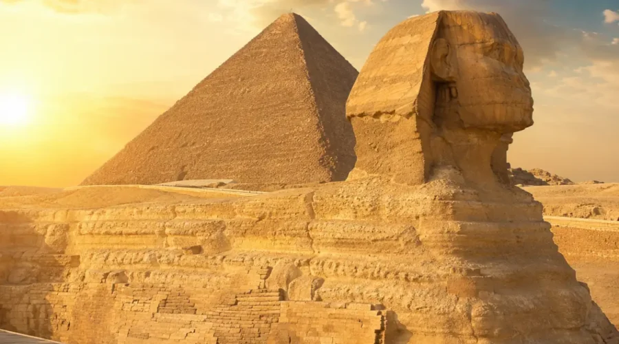 Great Sphinx of Giza with the Pyramid of Khafre in the background under warm golden light in Egypt.