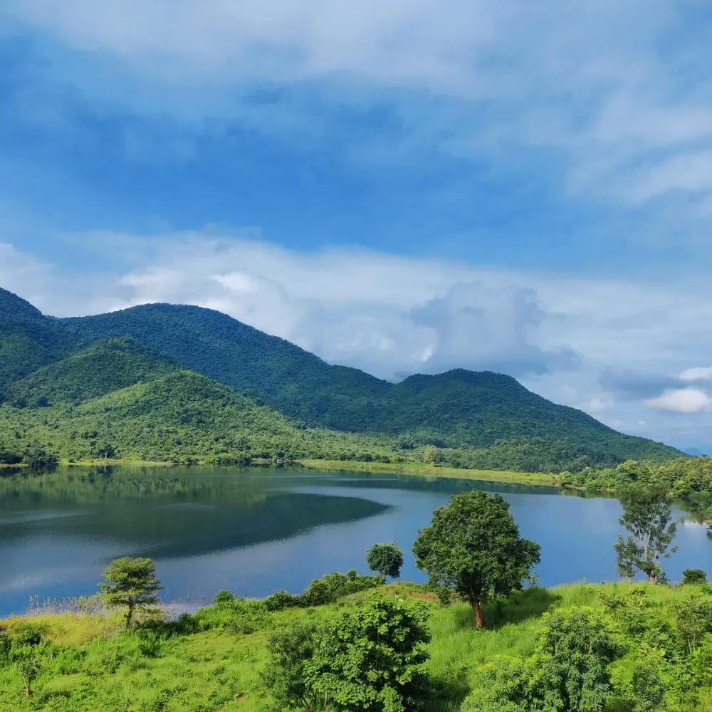 Grand Odisha Experience scenic landscape featuring a calm lake, lush green hills and peaceful natural beauty in Odisha